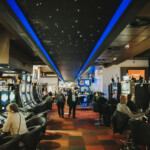 Une salle de casino animée avec des rangées de machines à sous de chaque côté de l'allée centrale. On voit plusieurs personnes qui sont assises sur des chaises noires en train de jouer aux machines.