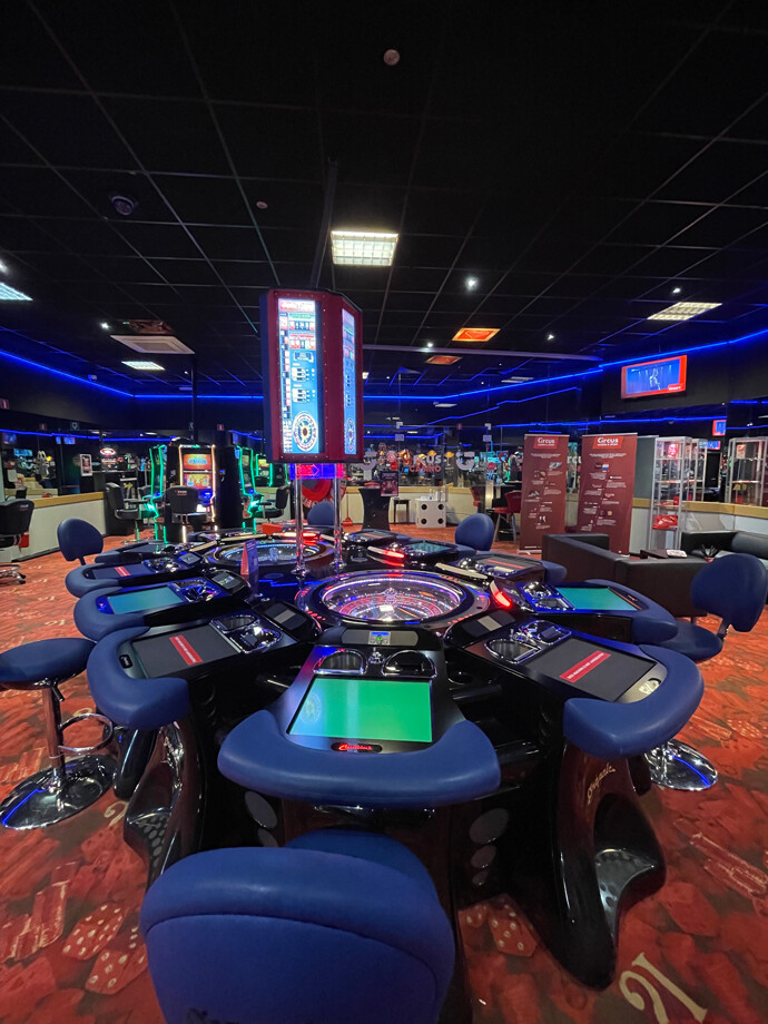 Une table de roulette électronique au centre avec des sièges bleus au casino de Boutersem.