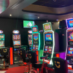 Une salle du casino de Fleurus avec des machines à sous illuminées aux couleurs vives. Les sièges noirs sont disposés devant chaque machine.