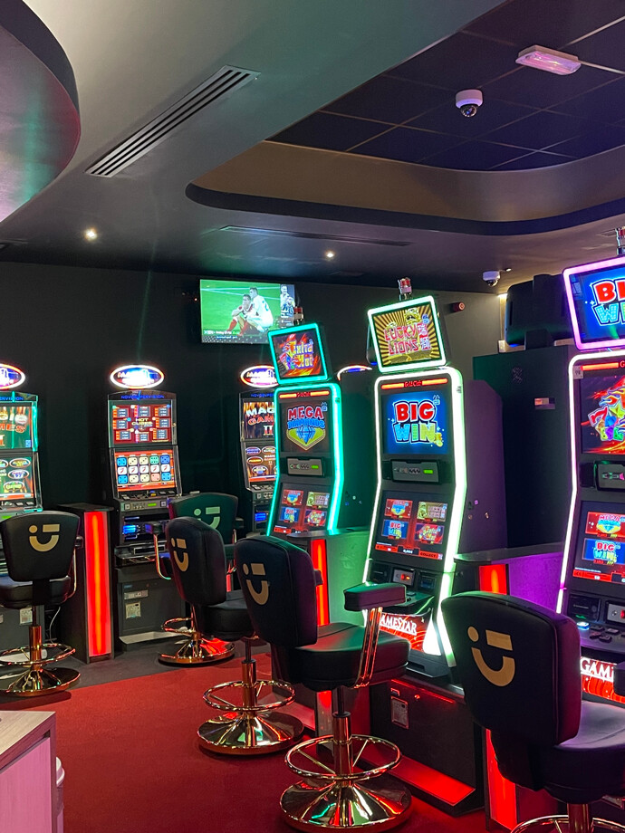 Une salle du casino de Fleurus avec des machines à sous illuminées aux couleurs vives. Les sièges noirs sont disposés devant chaque machine.