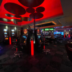 Vue de la salle de casino de Rocourt avec un plafond décoratif éclairé en rouge. Au centre, il y a des machines à sous entourées de chaises noires.